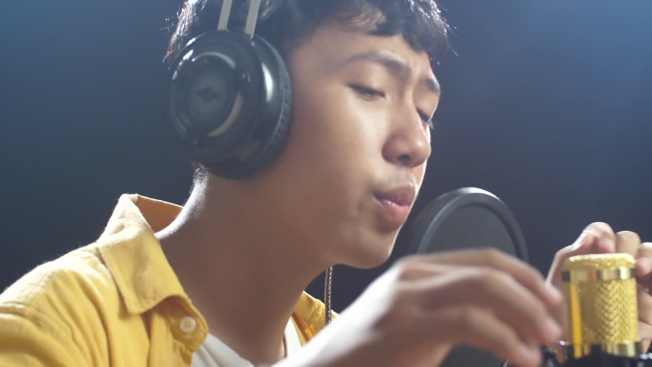 젊은 아시아 소년의 가까운 사진. 헤드폰을 들고 검은 바탕에 있는 응축기 마이크를 하고 있습니다.