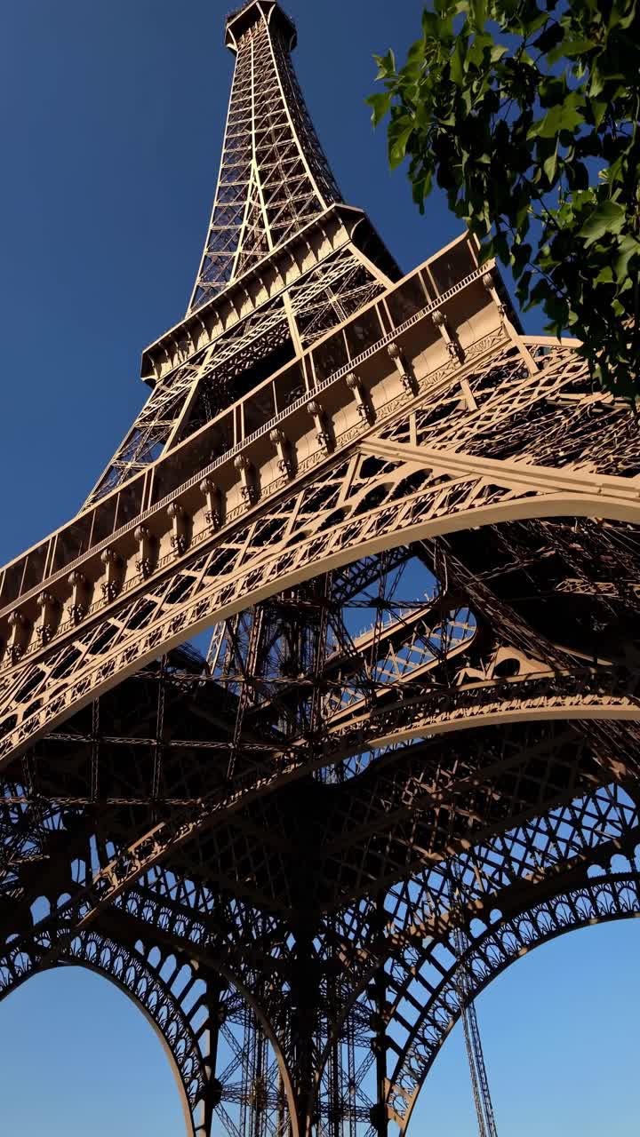 Low-angle video shot of the Eiffel Tower against a clear blue sky, capturing its intricate iron