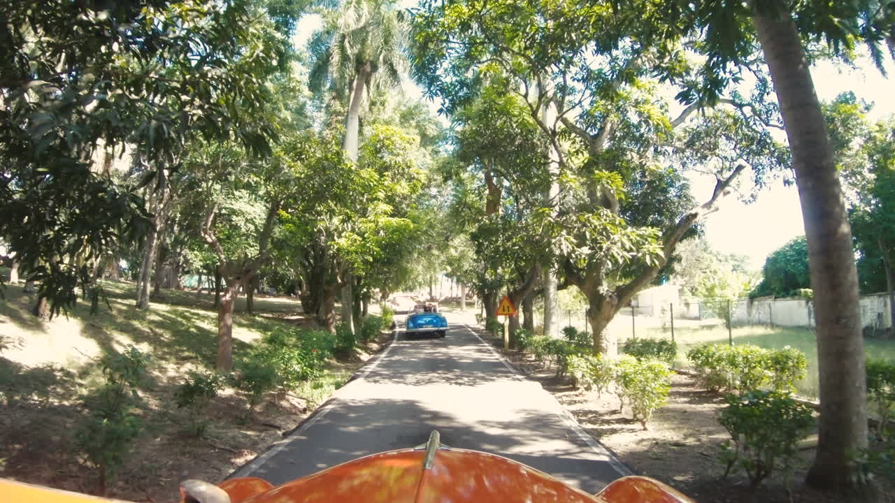 Punto di vista dall'esterno di una vecchia auto che percorre una strada a Cuba.