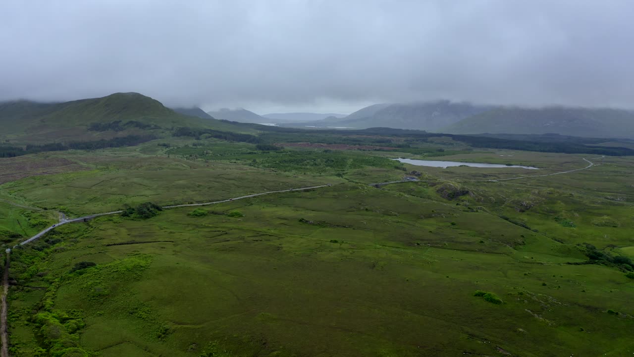 Western Way, Leenane, Connemara, County Galway, July 2021. Drone faces east while slowly tracking south following the course of a country road as low-hanging clouds drift across the mountains