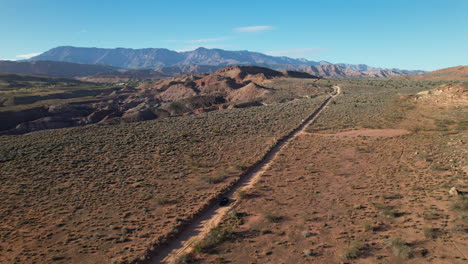 aerial shot of an suv driving along a straight dirt road in the utah desert, framed by expansive wilderness and distant mountains under a clear blue sky.