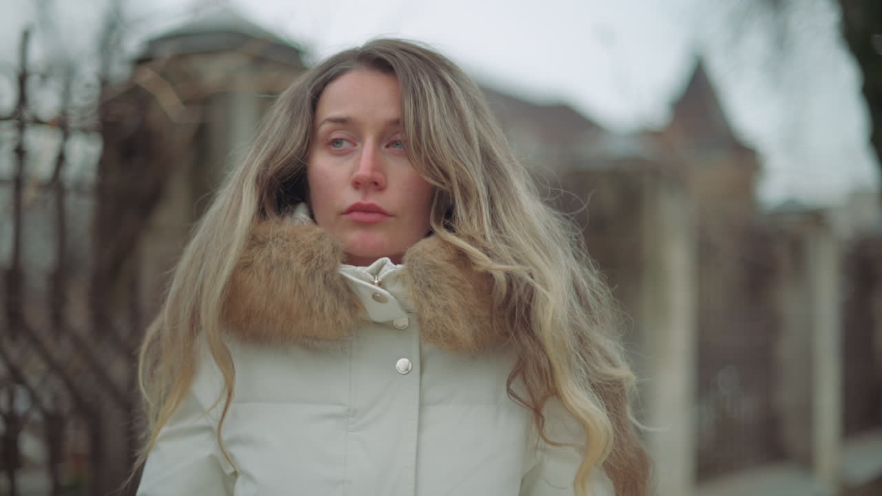 Close up of a pensive woman standing outdoors on a cold day, wearing a white winter coat with a fur collar