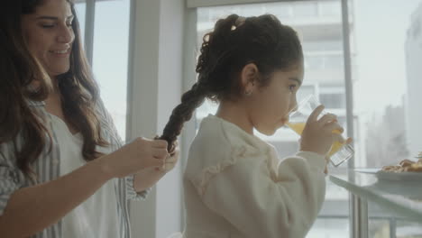 loving mother braiding hair of little daughter at home