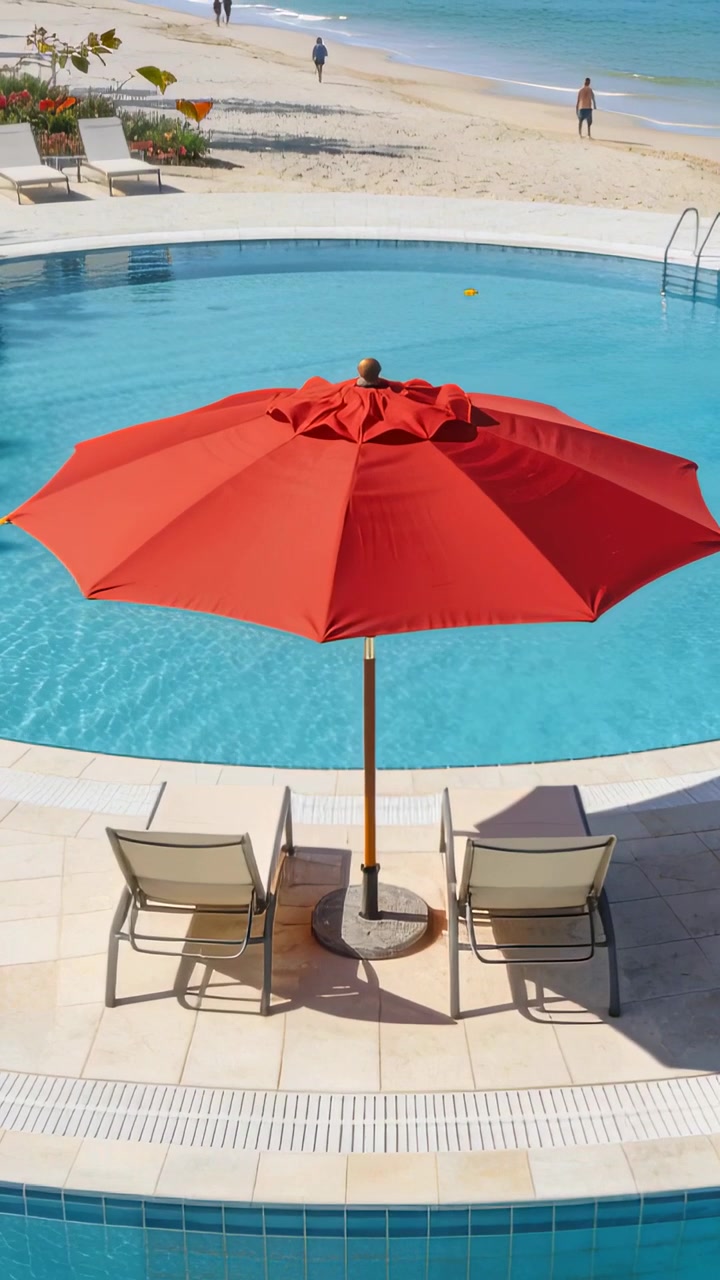 Video verticale: Brezza che fa ondeggiare un ombrellone rosso, ombreggiando due sedie a bordo piscina mentre adulti camminano per svago.