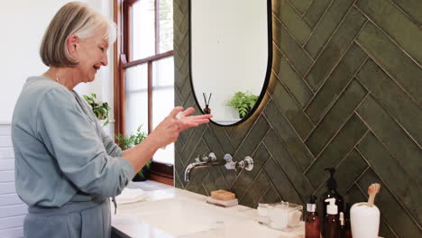 applying skincare, senior woman in bathroom with self-care routine essentials, at home