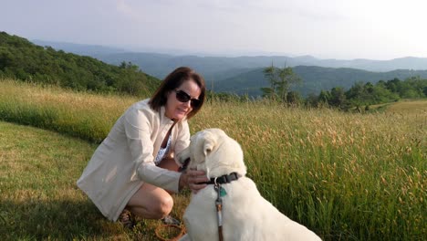 Breite-Aufnahme-Einer-Frau,-Die-Mit-Weißem-Labrador-Hund-Vor-Bergkulisse-Spielt