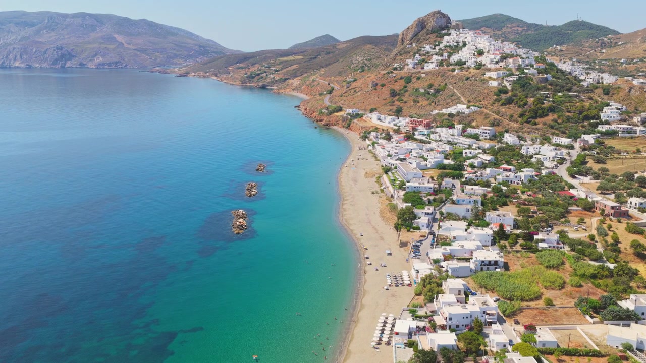 Yunanistan'ın Syros adasındaki Galissas Plajı'nın geleneksel beyaz Kiklad mimarisi, tertemiz kumlu kıyıları ve Ege Denizi'nin büyüleyici turkuaz sularını içeren görkemli havadan görünümü.