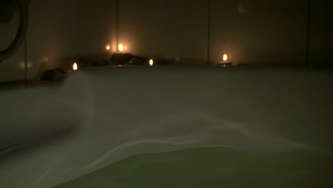 la luz se refleja en las ondas en la bañera con velas en segundo plano.