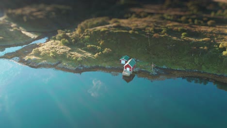 a small red boathouse and barn on the rocky coast of the fjord