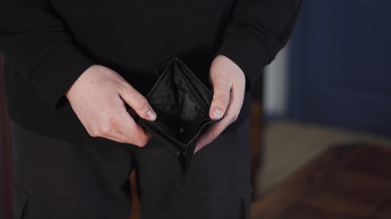 Broke man opens an empty wallet with no cash, showing financial crisis, debt, and money shortage in a close up view