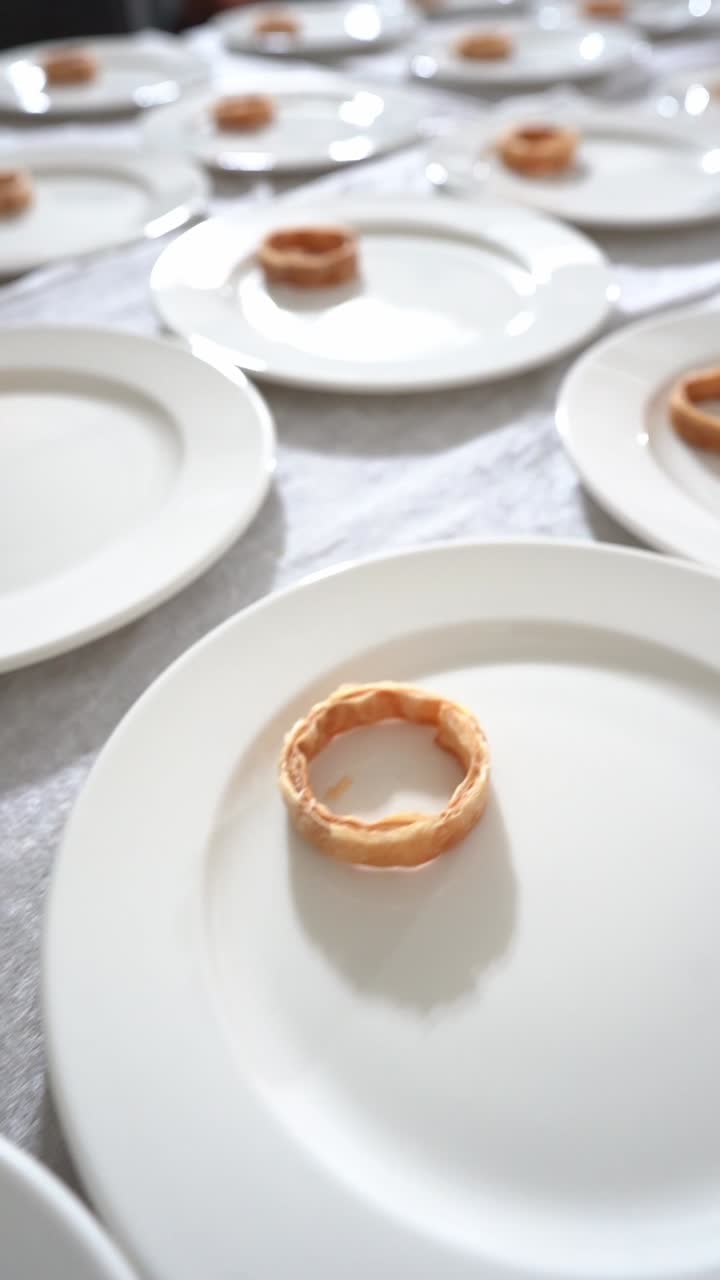 Minimalist fine dining setup with white plates arranged in rows, each holding a small pastry, close up shot