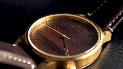 primer plano de un reloj dorado de lujo con esfera de madera y fondo negro