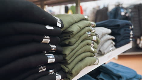 view of neatly folded clothes in various colors with size tags (s, m, l, xl, xxl) displayed on shelves in a mall. captured with a handheld camera, emphasizing the organized retail environment