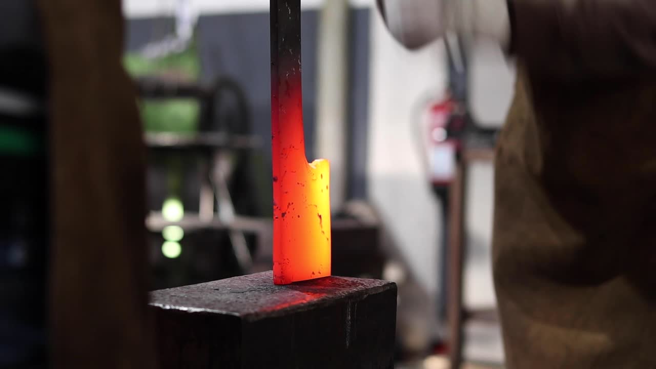 Blacksmiths forging hot metal with hammer in workshop
