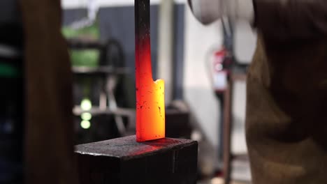 blacksmiths forging hot metal with hammer in workshop