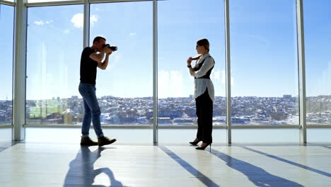 young business woman posing on camera in office. photographer taking photos of a girl wearing black and white costume against panoramic window with a city landscape.