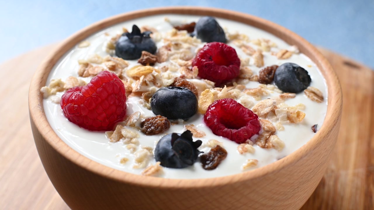 Yogurt con frutti di bosco e muesli per colazione in una ciotola che ruota su sfondo blu