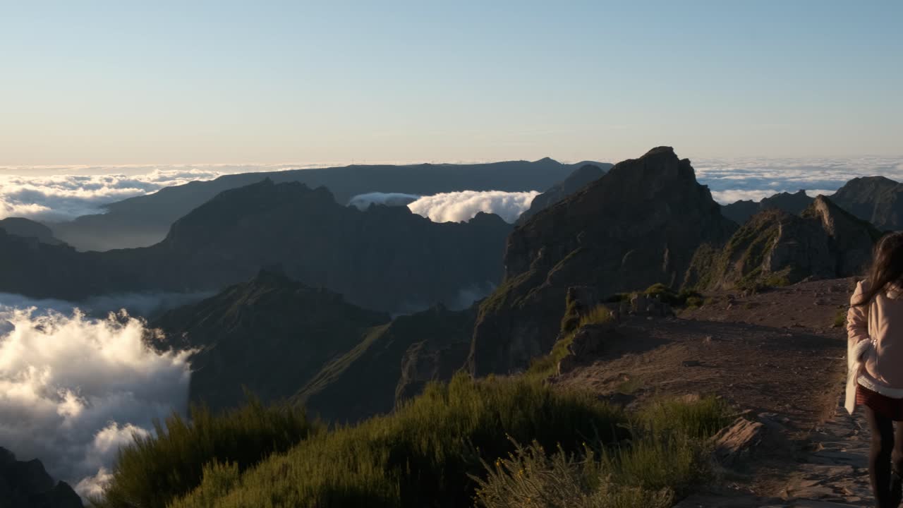 una joven asiática camina por un camino de piedra sobre las nubes en el sendero pico do ariero en madeira