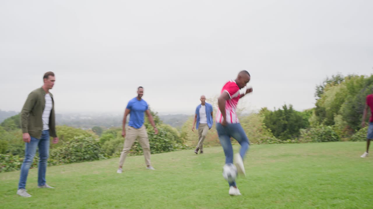 Diverse male friends passing, dribbling soccer ball on hill after teammate juggling for casual game