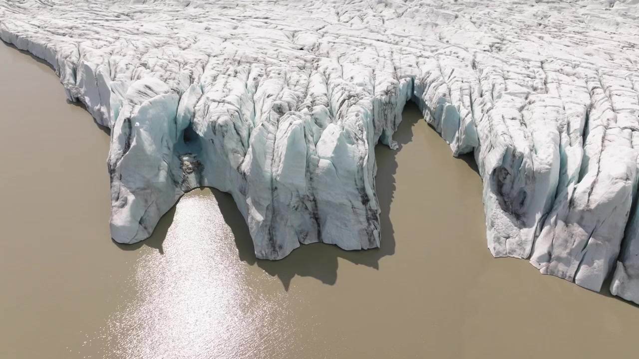 Vista aerea del bordo ghiacciato del ghiacciaio Fjallsjökull che incontra le acque serene della laguna glaciale Fjallsarlon, Islanda, evidenziando intricate fessure