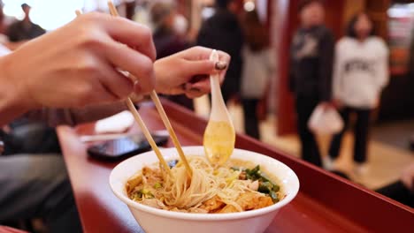 person enjoying noodles with chopsticks and spoon