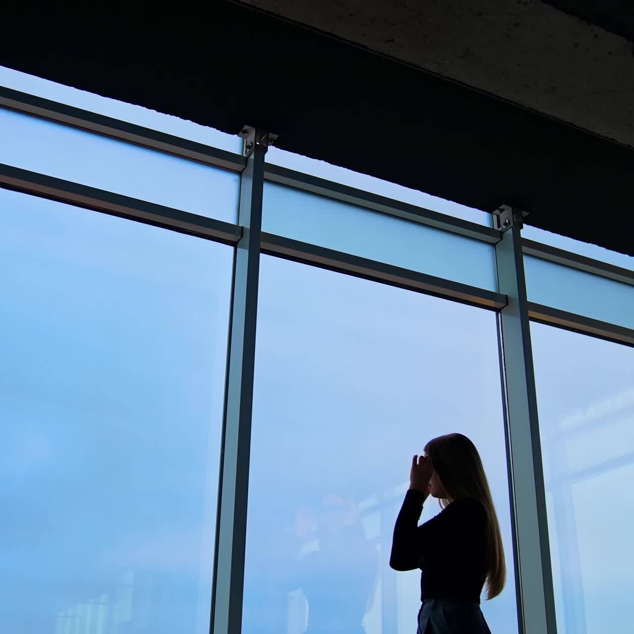 Business woman indoors. Tired female business worker in office putting off her glasses and looking through the large windows on blue sky background. Panoramic windows view