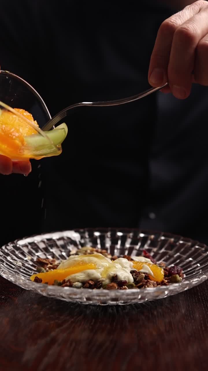 Hånd tilføjer friske appelsinskiver til skål med granola og yoghurt