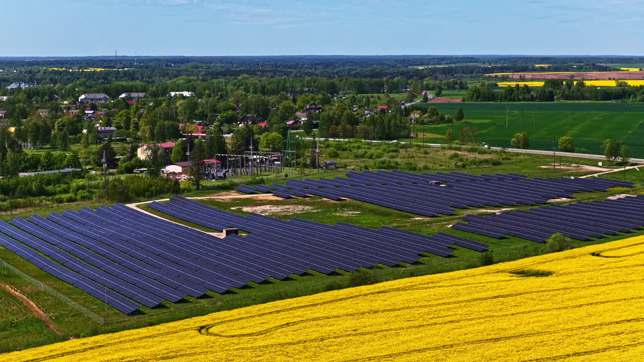 Drone video of large solar panel farm next to blooming rapeseed field and rural village