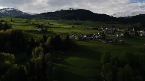 An-aerial-perspective-captures-a-quaint-residential-settlement-embraced-by-the-verdant-beauty-of-Obersaxen,-Graubünden,-Switzerland,-revealing-the-tranquility-of-alpine-living