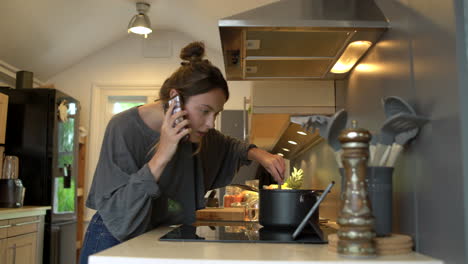 low angle shot of young woman on phone whilst cooking