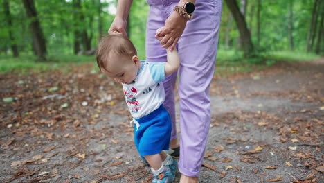 curious sweet baby boy walking with mom's help. lovely kid stepping and looking down with interest. nature backdrop.