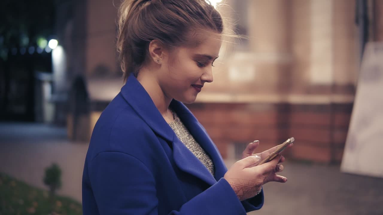 Beautiful young woman using her smartphone late at night in the city. Attractive girl texting, surfing on internet. Night