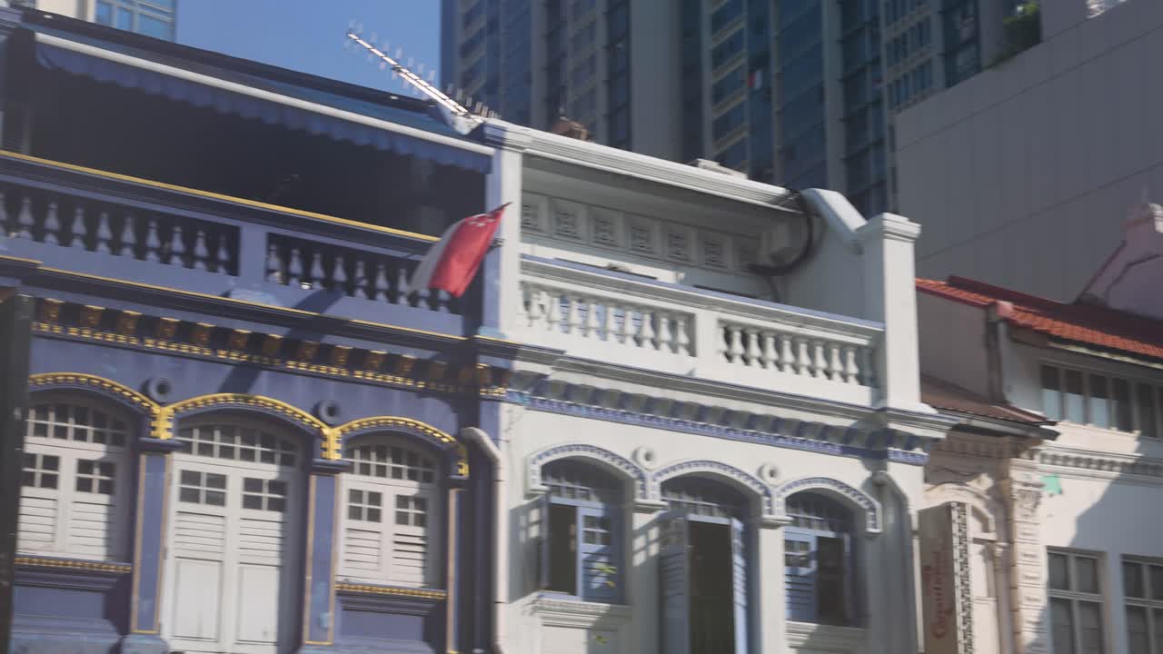 Camera moves past colorful colonial shophouses in daylight, highlighting architectural details and urban environment