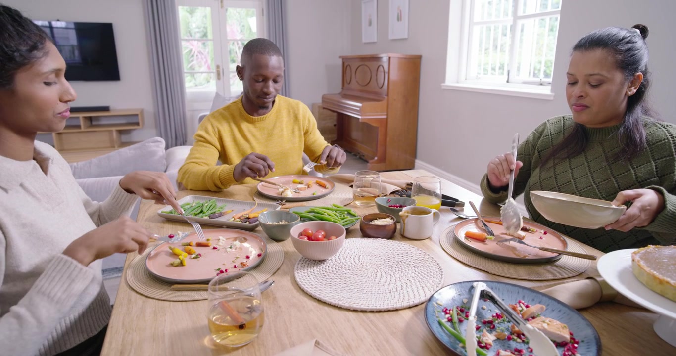 Famille riant, passant des bols et servant de la purée de pommes de terre à table à la maison, partageant le dîner.