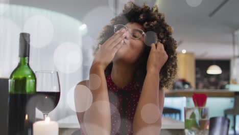 Animation-of-spots-over-african-american-woman-drinking-wine-and-having-video-call
