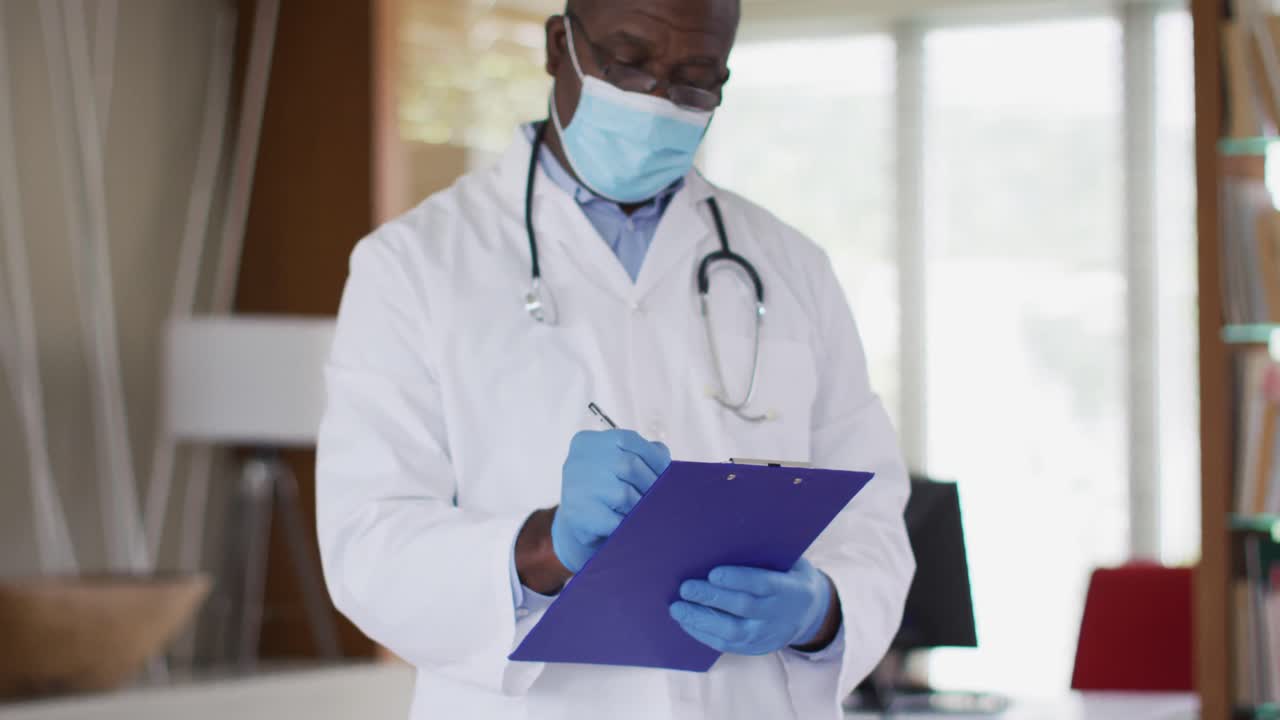 African american senior male doctor wearing white coat writing in notebook