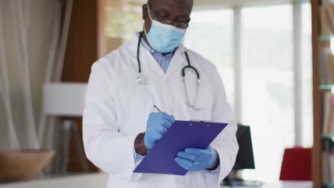 african american senior male doctor wearing white coat writing in notebook