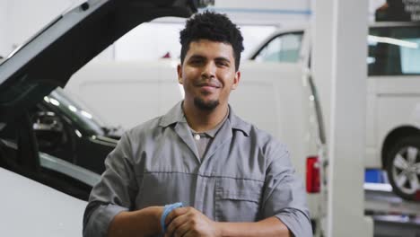 mecánico de automóviles afroamericano limpiándose las manos con un trapo y mirando a la cámara