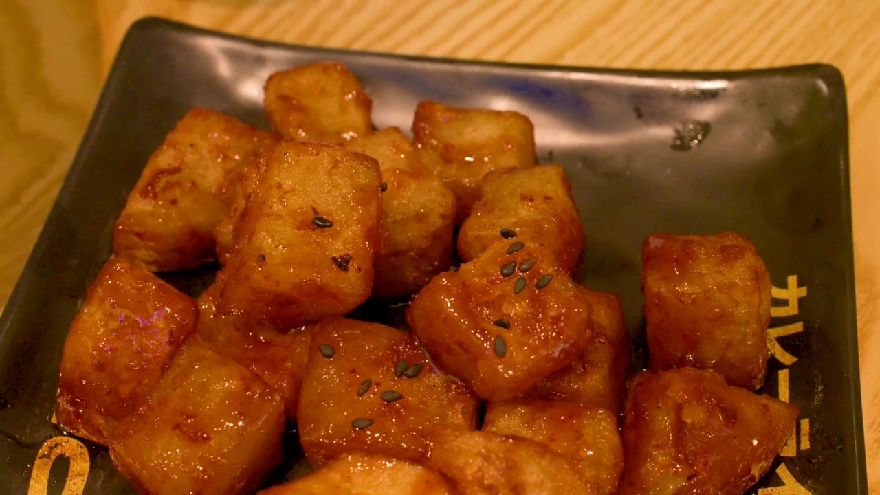 Primer plano estático de cubos de pollo glaseados crujientes servidos en un plato de cerámica oscuro.