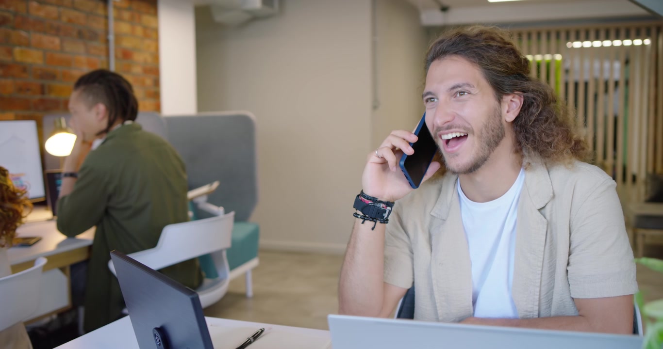 Forskellige kolleger ser en mand besvare et indgående opkald på kontoret, gestikulerende med en blå telefon.