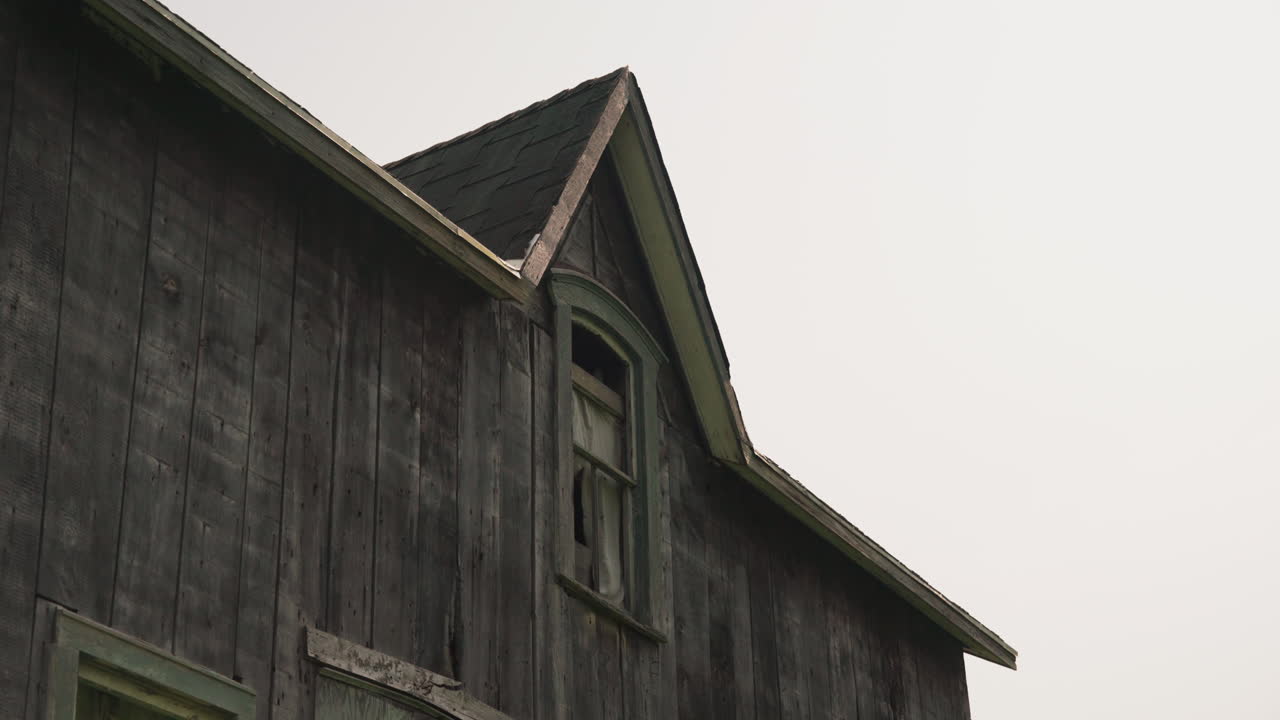 Wind blowing ripped curtain covering wooden window of abandoned home, medium