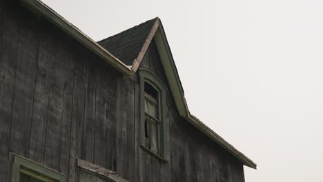 Wind-blowing-ripped-curtain-covering-wooden-window-of-abandoned-home,-medium