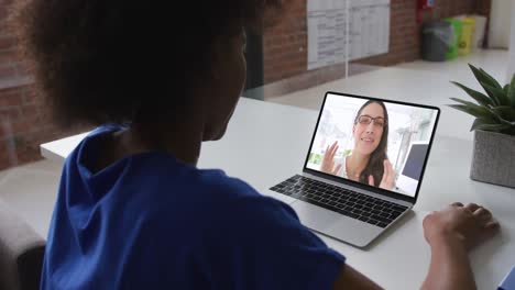 Back-view-of-african-american-woman-having-a-video-call-with-female-colleague-on-laptop-at-office