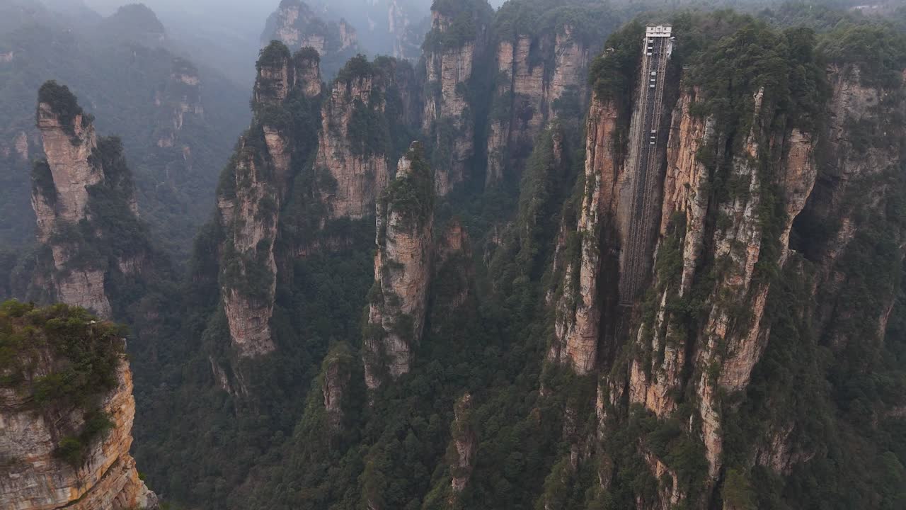 Rising high above the forest, the towering sandstone columns of Zhangjiajie showcase the impressive Bailong Elevator amidst breathtaking, mist-laden mountains.