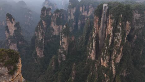 rising high above the forest, the towering sandstone columns of zhangjiajie showcase the impressive bailong elevator amidst breathtaking, mist-laden mountains.