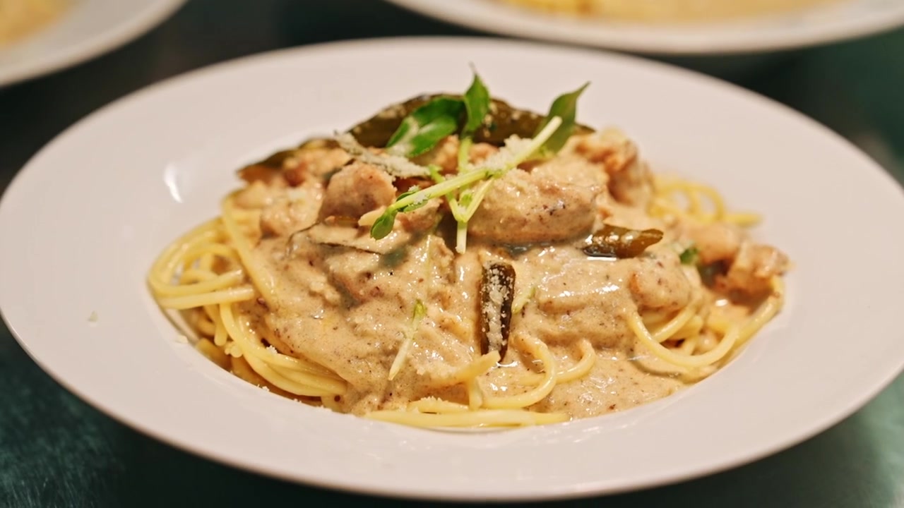 Carrellata ravvicinata che si muove su diversi piatti bianchi di pasta cremosa mentre uno chef li guarnisce con cura con erbe aromatiche e parmigiano grattugiato