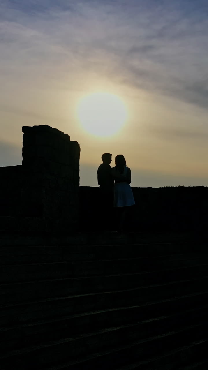 Lovely girl and her boyfriend meeting in an old castle near the river at dusk. Young beautiful couple standing together in the evening near lake. Vertical video