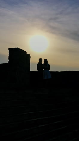 lovely girl and her boyfriend meeting in an old castle near the river at dusk. young beautiful couple standing together in the evening near lake. vertical video