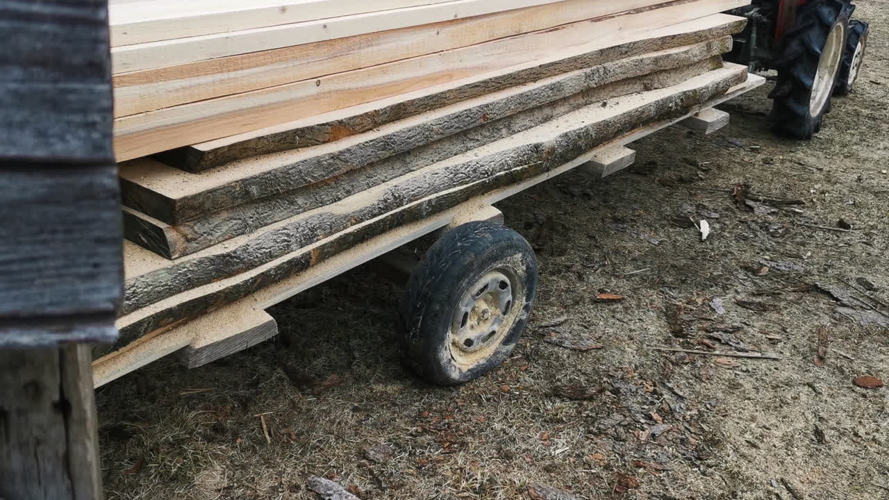 tablas de madera recién aserradas transportadas fuera del aserradero por un remolque de tractor rojo
