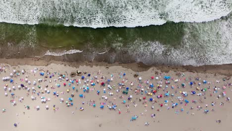 Vista-Aérea-De-Pájaro-Sobre-La-Playa-De-Maitencillo-Con-Bañistas-Y-Coloridas-Sombrillas,-Olas-Rompiendo